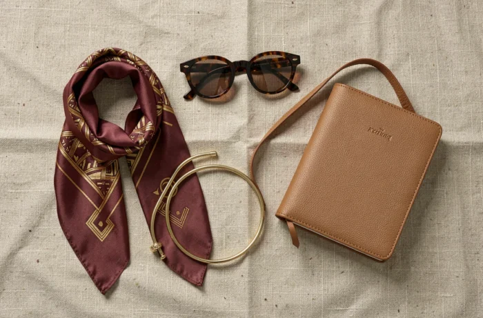Flat lay d'accessoires de mode tendance 2024 sur fond de lin : foulard en soie, lunettes écailles, bracelet doré et sac en cuir