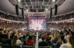 Vue panoramique de la Bercy Arena depuis les gradins intermédiaires lors d'un concert, avec le public et les systèmes de sonorisation suspendus visibles